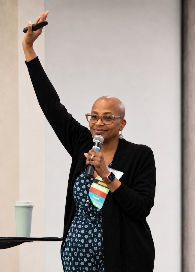 Edie Clarke speaking to an audience with a microphone and raising her hand