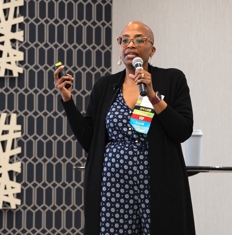 Edie Clarke speaking at an event with a microphone and presentation clicker
